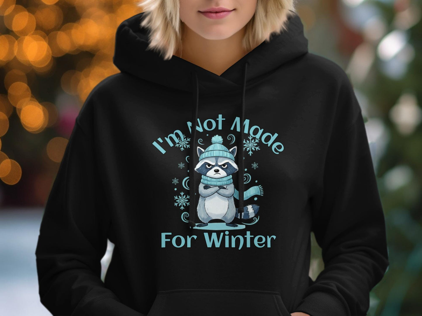 Person wearing a black hoodie with a graphic of a raccoon and text 'I'm Not Made For Winter' against a blurred outdoor background.